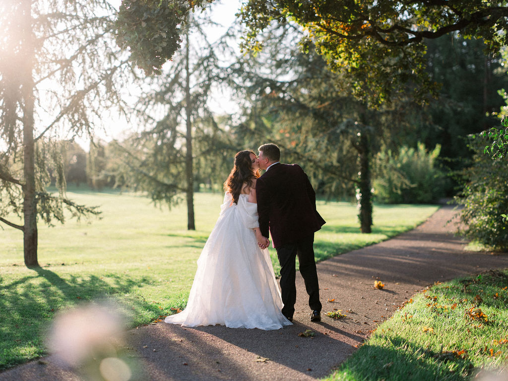 Bride and groom kiss under the trees at sunset near the river