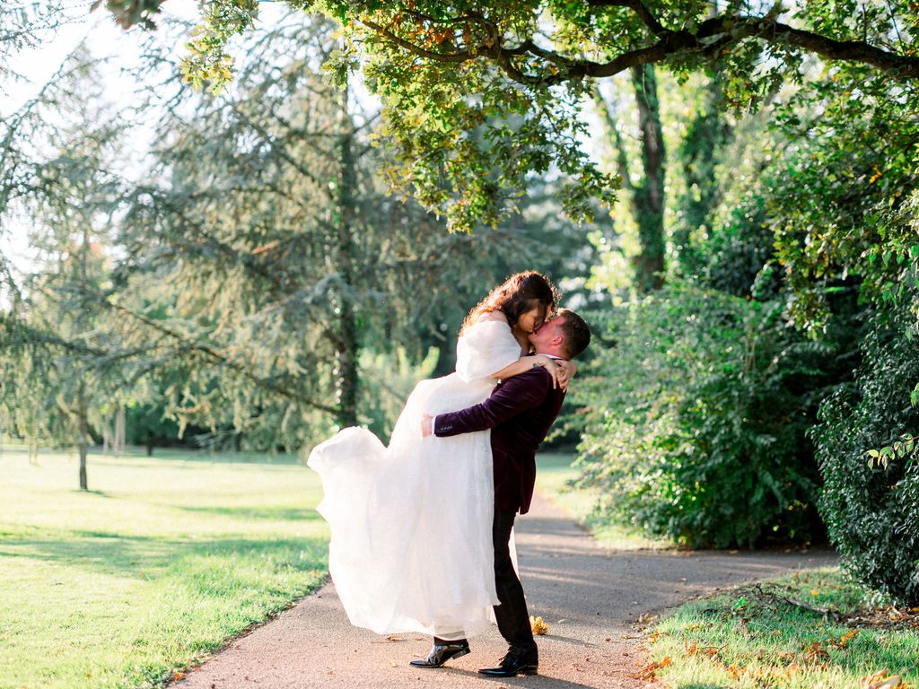 Groom lifts the bride in a romantic kiss under a tree-lined path