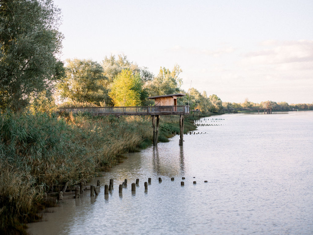 Wooden fishing hut on stilts overlooking a peaceful river at sunset